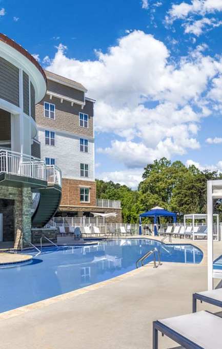 A large swimming pool is surrounded by a white fence and chairs.