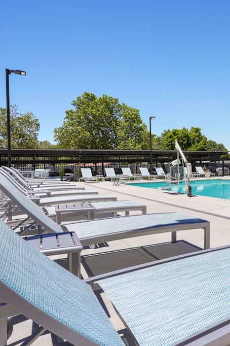 A sunny day at the pool with lounge chairs and a building in the background.