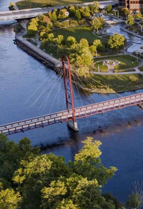 A red suspension bridge spans a river in a city.