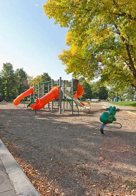 A playground with a red slide and a child on a bicycle.
