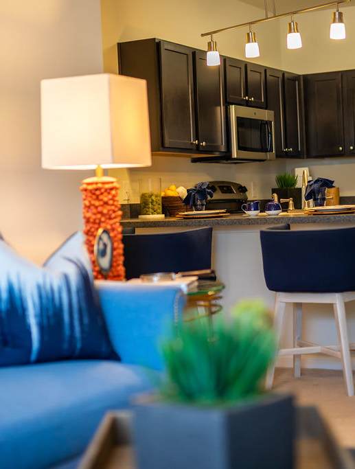 A blue couch sits in a kitchen with a white refrigerator and black cabinets.