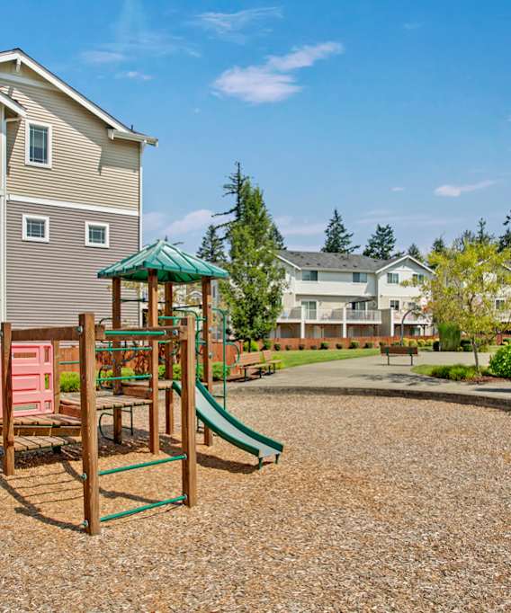 A playground with a green slide and a red swing set in front of apartment buildings.
