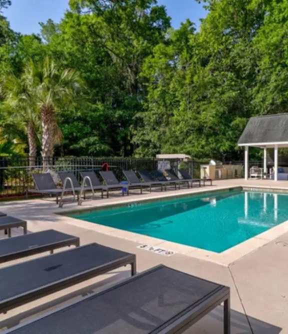 A pool surrounded by trees and lounge chairs.