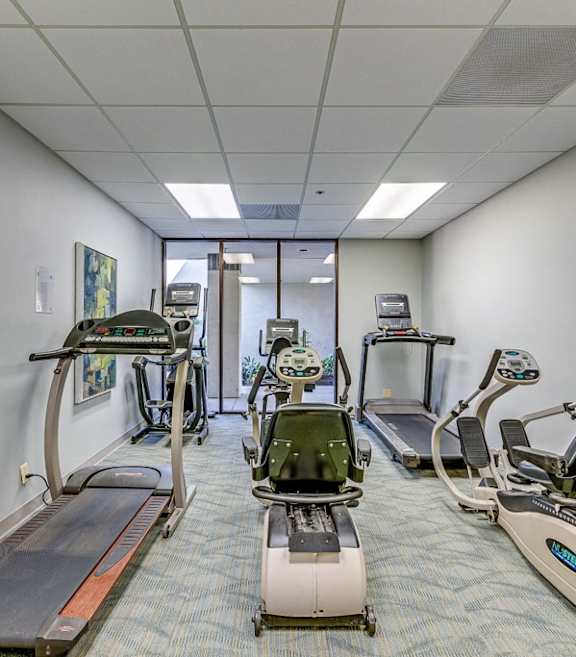 A row of treadmills and elliptical machines in a gym. at Legacy Hills at Poway 55+ Apartments, Poway, California