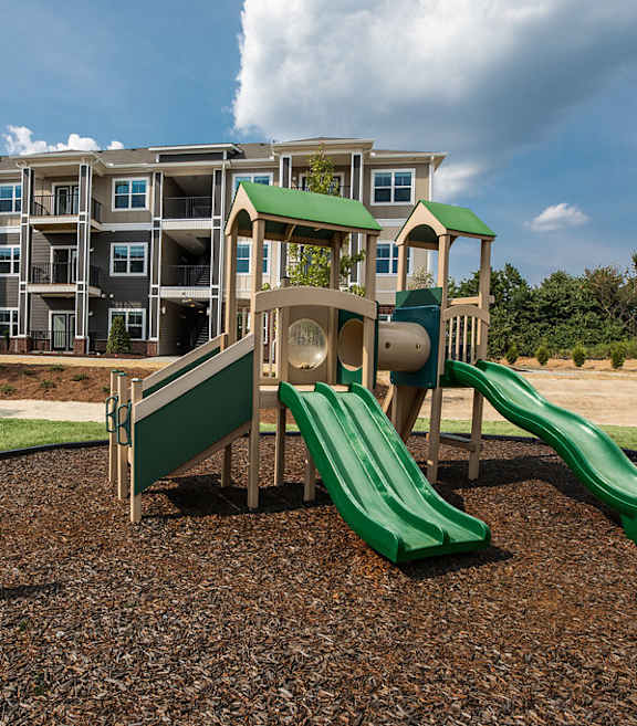 A playground with a green slide in front of apartment buildings.