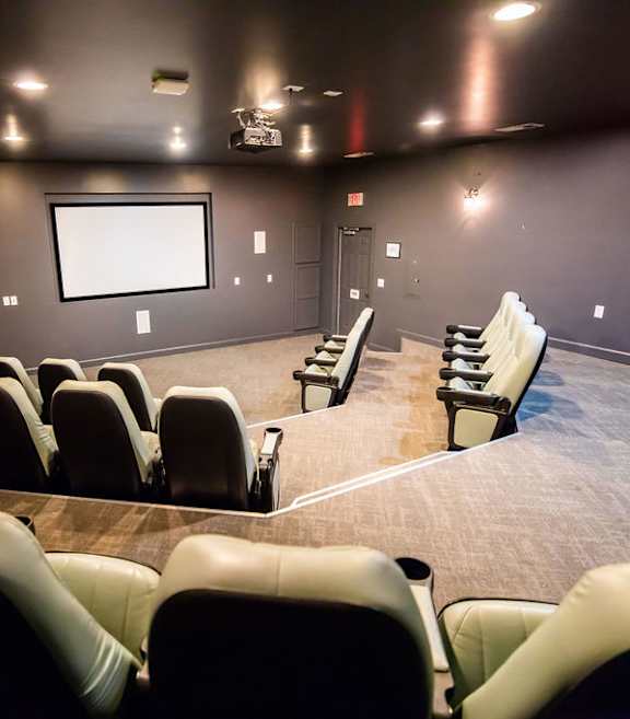 A dark cinema room with rows of seats facing a large screen.
