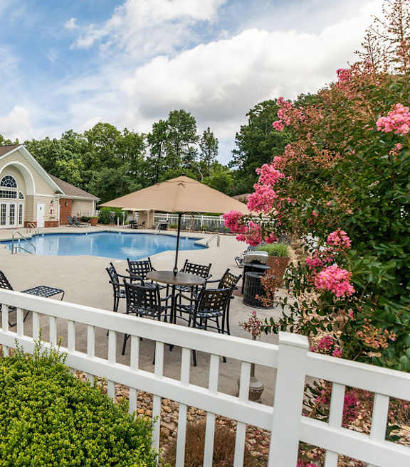 A white picket fence with a lamp post in front of a house with a pool.