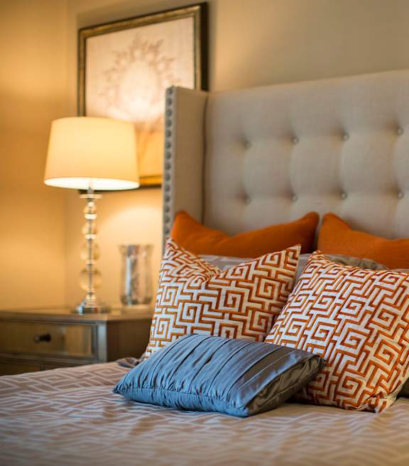 A bed with a white headboard and orange and grey pillows.