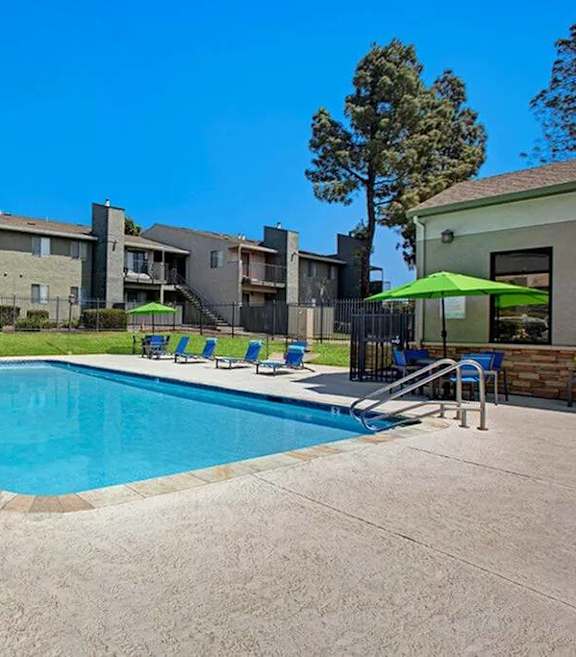 A swimming pool surrounded by chairs and umbrellas in front of apartment buildings at The Henley Apartments, Suisun City, CA, 94585