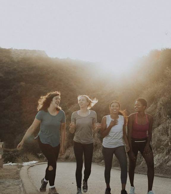 Four women running on a road with sunlight shining through the trees.