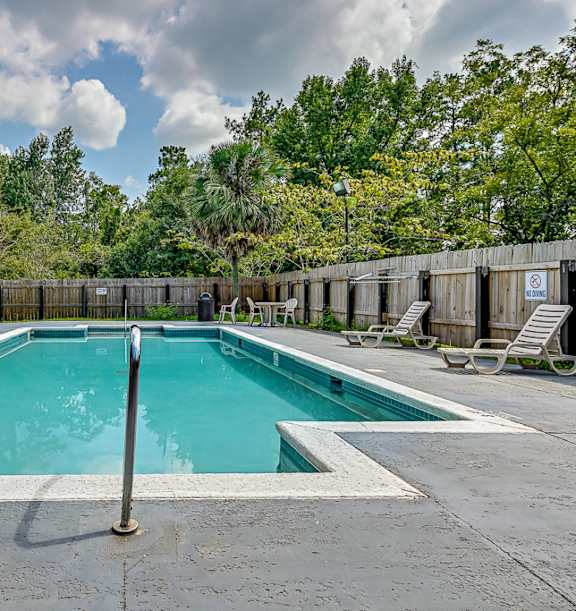 A large outdoor swimming pool surrounded by a wooden fence and lounge chairs.