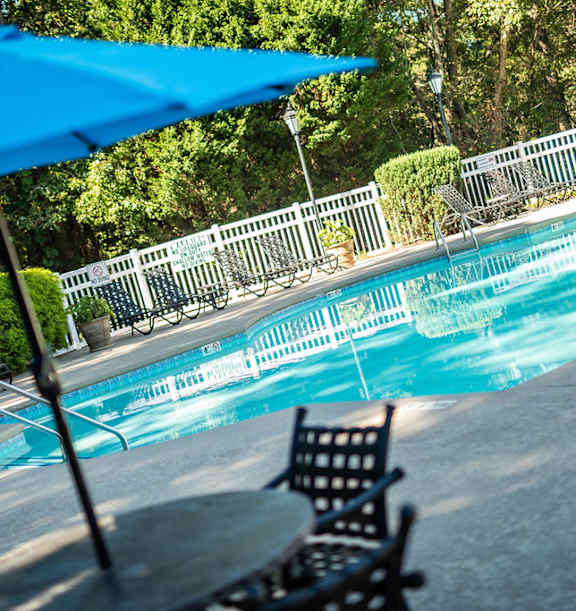 A blue umbrella is over a table by a pool.