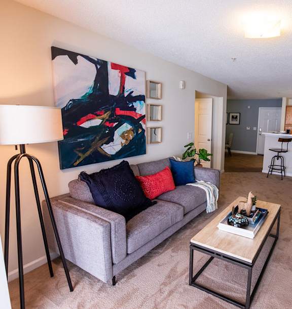 A living room with a grey couch and a painting on the wall.