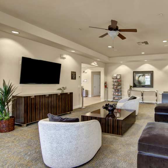 A large community room with couches, a coffee table, bookshelves, and plush chairs at Bela Rosa. 