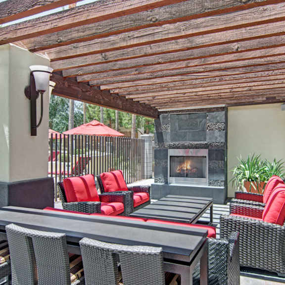 A patio with a fireplace with chairs with red cushions and tables at Natura Villas Apartment Homes. 