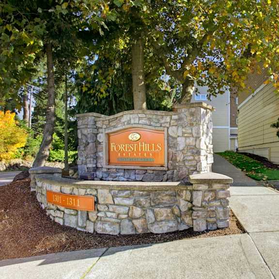 The exterior of the tan and brown apartment buildings and parking lot at Forest Hills Estates. 