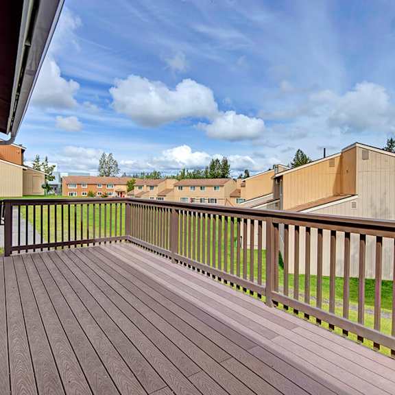 A brown wooden patio with a view of the light orange apartment homes at the Glen Apartment Homes. 