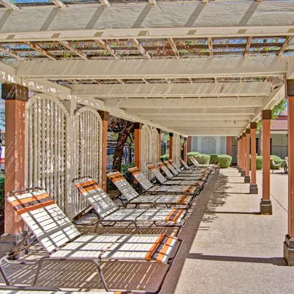 A covered patio with lounge chairs near a swimming pool at Motif Apartment Homes. 