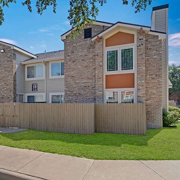 The exterior of an apartment building with a wooden fence in front of it and a grass lawn at Summertree Place Residences. 