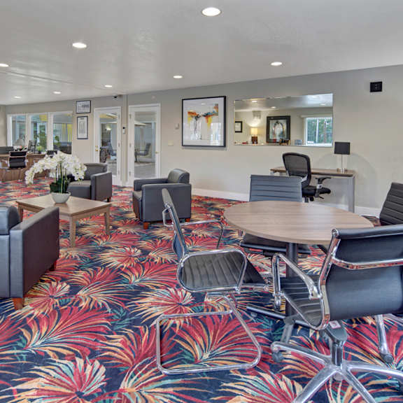 The amazing resident lounge with couches, decorations, large windows, unique overhead lighting, the leasing office with a desktop, table and chairs, a desk and chair, black leather chairs, and coffee tables at the Club at Eagle Point Apartment Homes. 