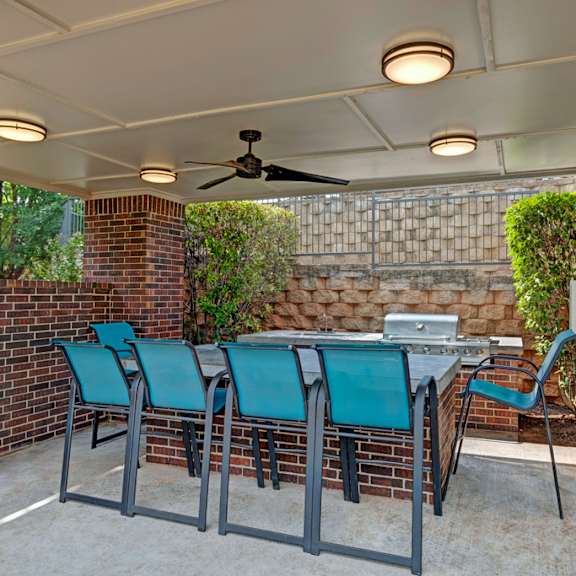 A patio with a table, chairs, a grill, and a ceiling fan at Lincoln at Central Park.