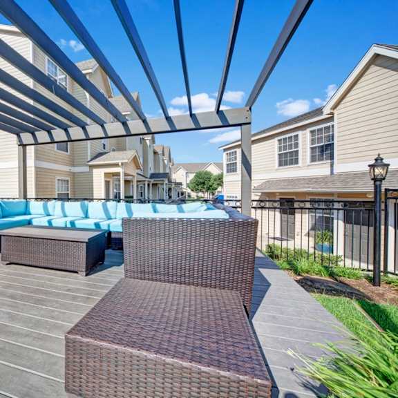 An outdoor resident patio with greenery and coffee tables and bright blue chairs surrounded by the apartment buildings at Summit Pointe Apartment Homes. 