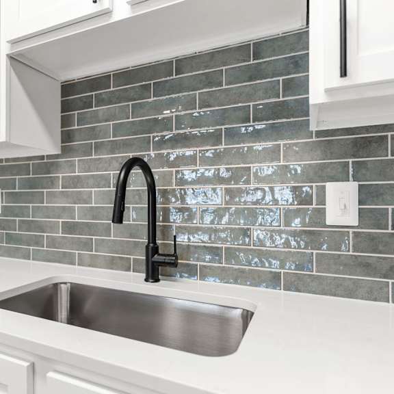 A kitchen with a sink and a grey tile backsplash.
