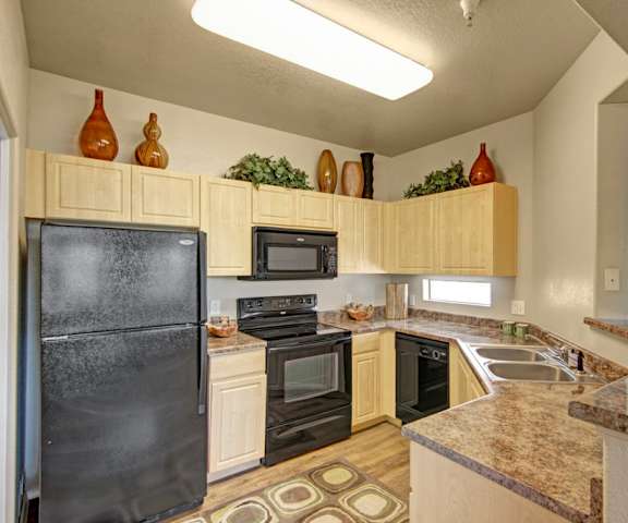 A large kitchen with black appliances, marble countertops with ample space, and spacious wooden cabinets with decorations at Natura Villas Apartments. 