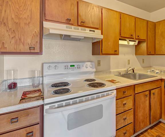 A cozy kitchen with white appliances, kitchen utensils, overhead lighting, light countertops with lots of room, and large wooden cabinets at the Alaskan Apartment Homes. 