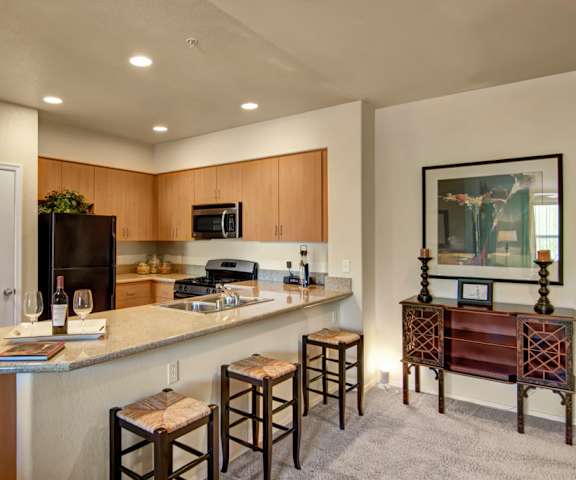 A kitchen with appliances, an island, and stools at Bela Rosa Apartments. 