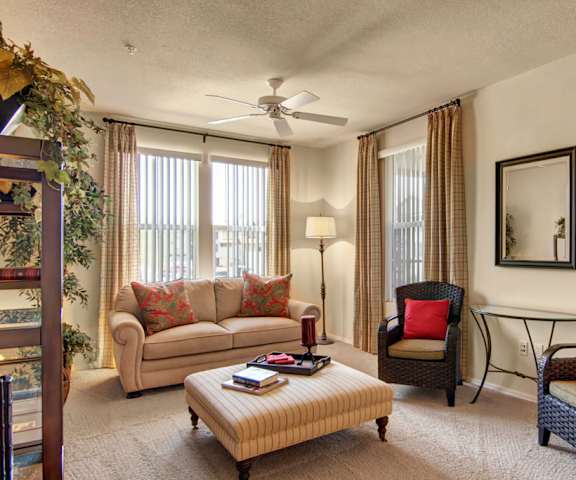A living room with a couch, coffee table, chairs, and windows at Bela Rosa Apartments. 