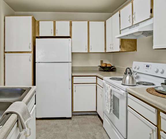 A kitchen with white appliances and counters at Breckenridge Apartments. 