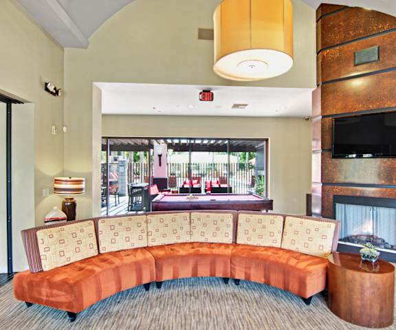The resident lounge with a fireplace, couches, TV, window and doors showing the pool area, decorations, plush chairs, and coffee tables at Natura Villas Apartments. 