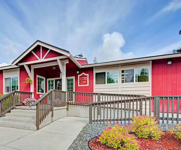 The bright red leasing office with bushes and plants in the front and a staircase and wheelchair ramp at the Glen Apartment Homes. 