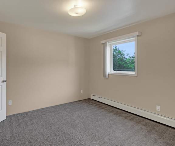 An empty carpeted bedroom with a window at La Maisonette Apartment Homes. 