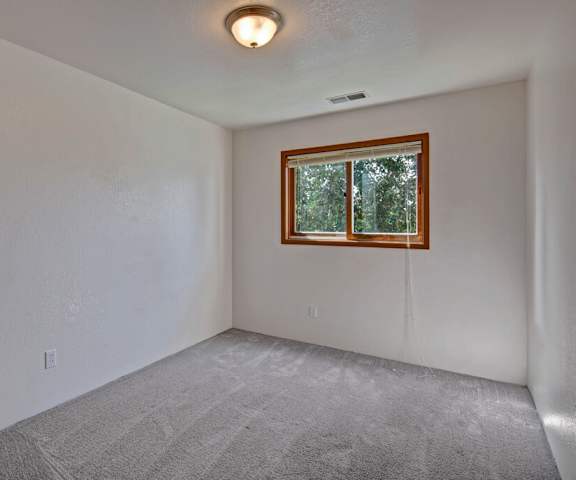 An empty carpeted bedroom with a window at the Legacy West Apartment Homes. 