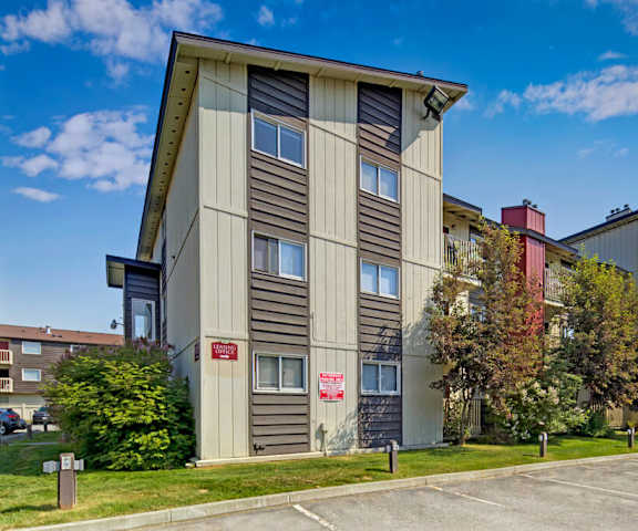 The exterior of the apartments and the green space with grass, trees, and shrubs at Legacy West Apartment Homes. 