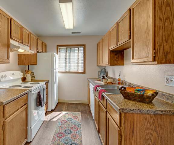 A cozy kitchen with white appliances, light counter, and spacious wooden cabinets at the Legacy West Apartments. 