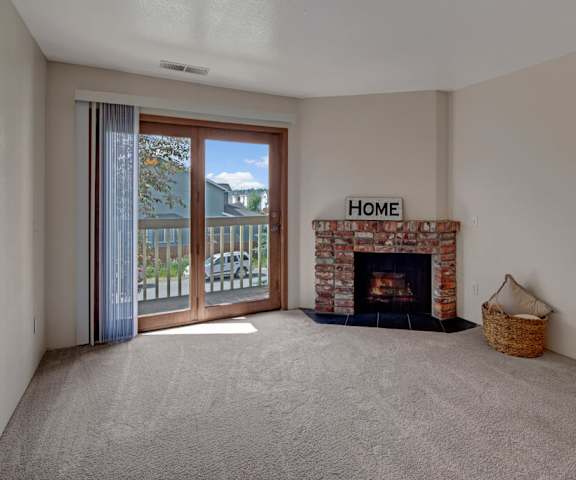 A large empty living room with carpeting, a fireplace, and the entrance to the patio at the Legacy West Apartment Homes. 