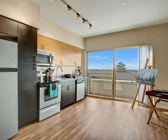 A kitchen with stainless steel appliances, marble countertops, and large wooden cabinets with doors to the balcony at Leilani Apartment Homes. 
