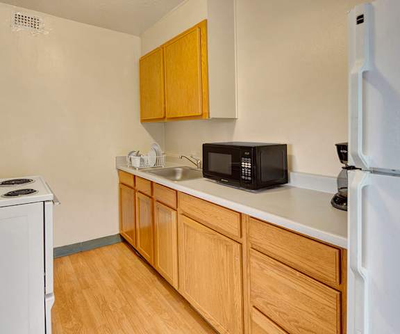 A cozy kitchen with white appliances, light counter with ample space, and spacious wooden cabinets at Mendenhall Tower Apartments. 
