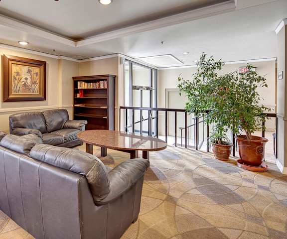 The resident lounge with a bookshelf, couches, decorations, plush chairs, stairs and door to the outside, and coffee tables at Mendenhall Tower Apartments. 