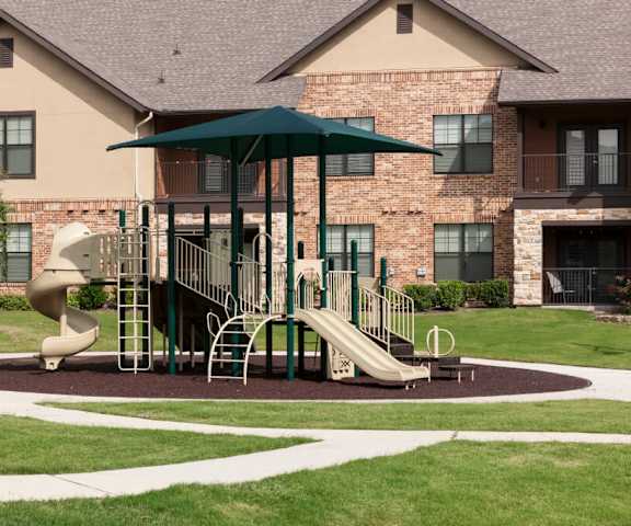 A playground with a green umbrella and a slide.