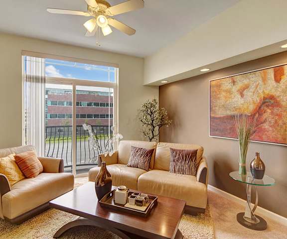 The amber living room with a couch, plush chairs, ceiling fan coffee table, decorations, a TV, and balcony at Park Plaza II Apartments. 