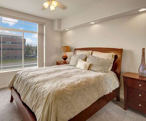 A large bedroom with a queen-size bed, a dresser, decorations, window, and nightstands at Park Plaza II Apartments. 