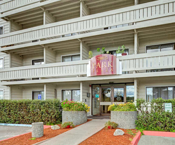 The entrance to the office at Park Plaza Apartments with a sign, a walkway leading up to it, surrounded by plants.