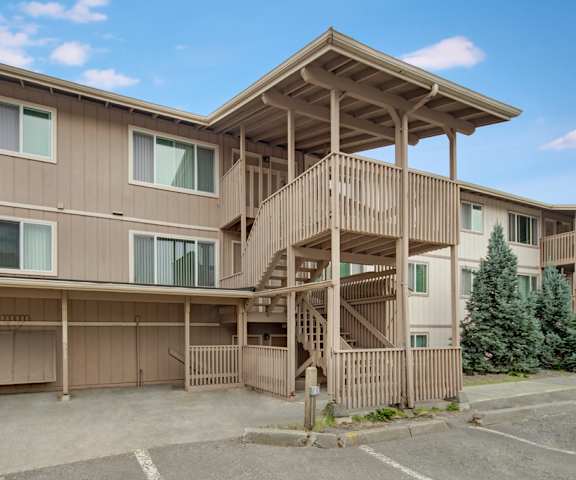 The tan exterior of Rancho Tudor Apartments with outdoor stairs and trees. 