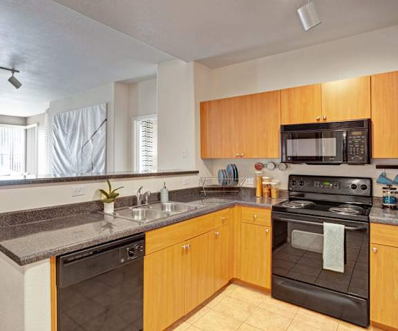 A spacious kitchen with black appliances, marble countertops, and wooden cabinets with decorations at Rio Paradiso Apartment Homes. 