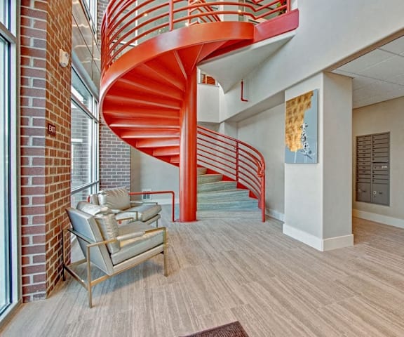 Part of the resident lounge with silver plush chairs, wall art, and a unique orange spiral staircase at the Ritz Classic Apartment Homes. 