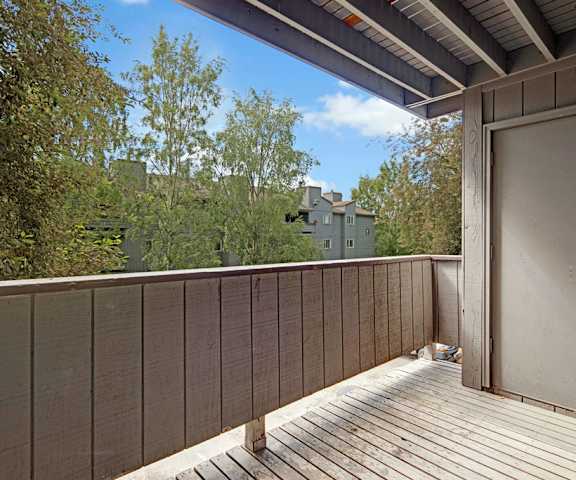A wooden balcony with the door to the apartment and a gorgeous view of the other apartment buildings at Russian Jack Apartment Homes. 